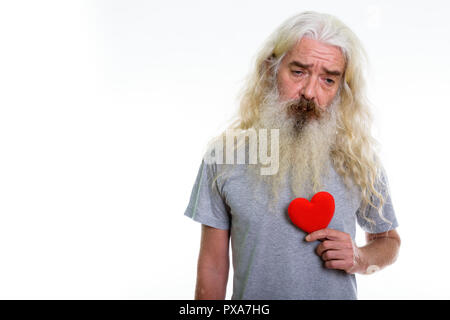 Studio shot of senior bearded man holding red heart while lookin Stock Photo