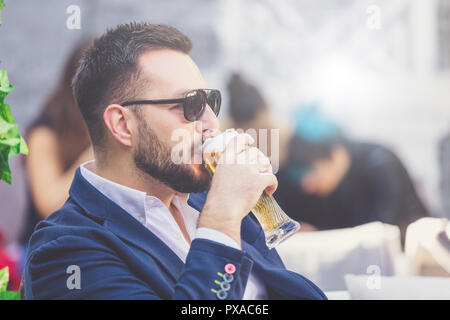 Portrait of fashionable man sitting in cafe pub outdoors and drinking beer. Stock Photo