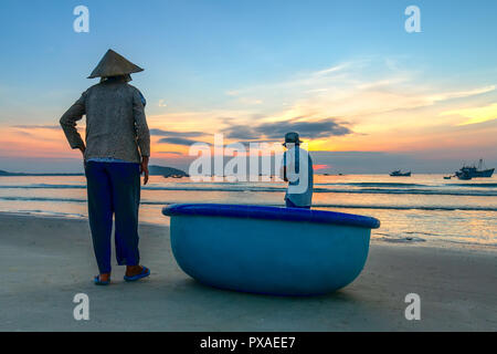 The elderly couple on a beautiful beach at dawn next to a basket boat looking to catch fishermen on shore hoping for a good harvest Stock Photo