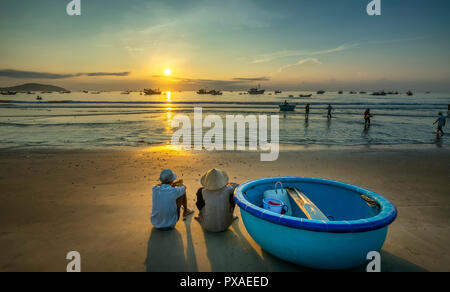 The elderly couple on a beautiful beach at dawn next to a basket boat looking to catch fishermen on shore hoping for a good harvest Stock Photo