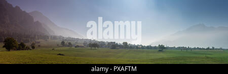 rural Swiss countryside landscape with farm fields and misty mountains and forest in late autumn Stock Photo