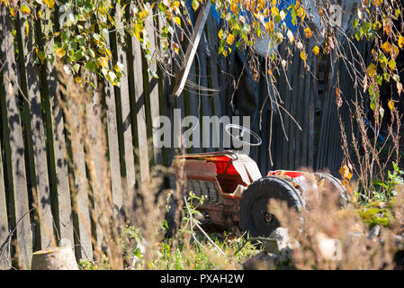 Picture from the past, old abandoned toy, old tractor, autumn in the countryside, pastoral picture, autumn trees, fence Stock Photo