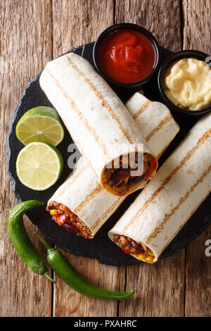 Fast food grilled burrito with beef and vegetables close-up on the table. Vertical top view from above, rustic style Stock Photo