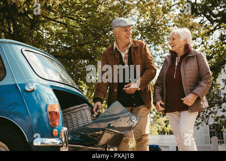 Old man and woman putting picnic basket in their car trunk. Senior couple going on picnic on a winter day. Stock Photo