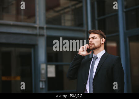 Businessman walking out of office and talking over cell phone. Businessman in formal clothes walking outdoors using mobile phone. Stock Photo