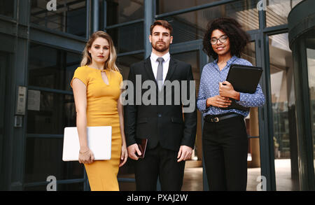 Portrait of three business people standing together in front of office building. Group of diverse business professionals looking at camera confidently Stock Photo