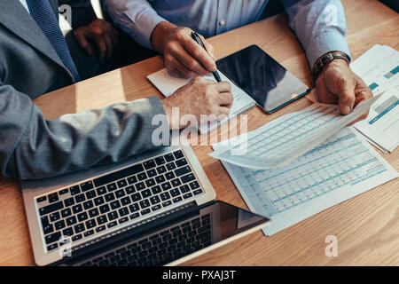 Close up of two businesspeople sitting at table with laptop working on reports. Cropped shot of business people analysing financial reports at cafe. Stock Photo