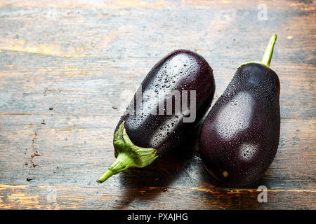 two ripe eggplants in drops of water. on a wooden table, close-up. place for text Stock Photo
