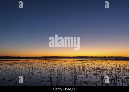 The sky is illuminated by the sun setting over the lake Stock Photo