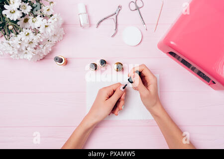 Festive composition process painting nails with gel nail polish near UV lamp, tools and flowers, top view. Female hand applying shellac top cover doin Stock Photo