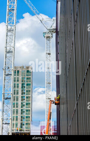 A worker on an aerial platform and tower cranes, at the Circle Square office and residential development, Oxford Road, Manchester, England, UK Stock Photo