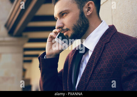 Handsome and fashionable man with a beard talking on the phone in close-up Stock Photo