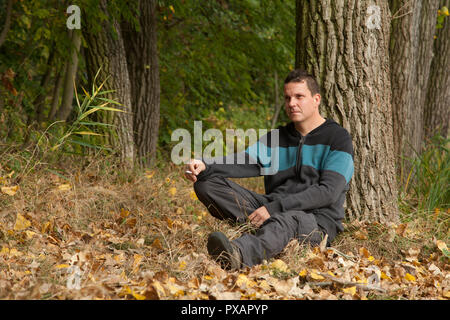Man sitting and smoking cigarette in autumn colorful weather in woodland. Weather: sunny and dry Stock Photo