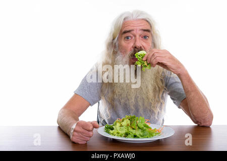 Studio shot of senior bearded man eating plate of salad on woode Stock Photo