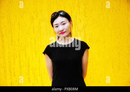 A chinese woman wearing a black shirt in front of a yellow wall. Stock Photo