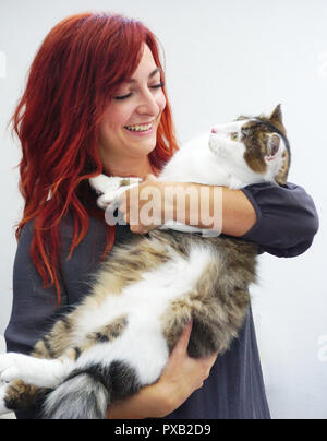 Red haired woman smiles while holding a big beautiful pedigree pet cat Stock Photo