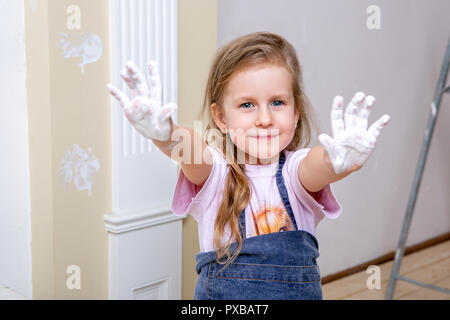 Repair in the apartment. Happy family mother and daughter in aprons paint the wall with white paint. The girl shows her palms in the paint and laughs. Stock Photo