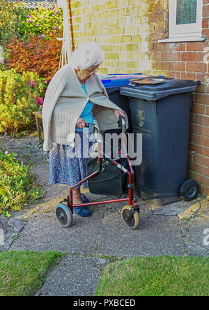 An elderly woman walking with the aid of a trike, 3 wheeled stroller, 3 wheel walking aid or 3 wheel walker, England, UK Stock Photo