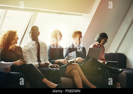 Diverse group of smiling businessmen and businesswomen sitting tgether on a sofa in an office discussing work Stock Photo