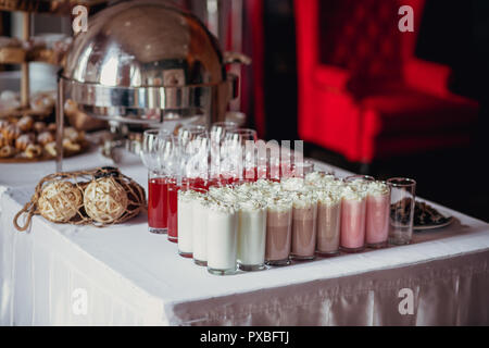 Candy bar on birthday party with a lot of different candies, cupcakes, souffle and cakes, milkshakes and juice in glass cups. Decorated on wooden stan Stock Photo