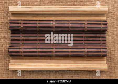 Dark and light bamboo mat in the form of a scroll lie on the burlap. Top view Stock Photo