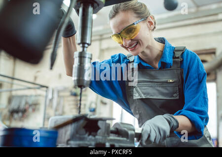 Woman worker in metal workshop using pedestal drill Stock Photo