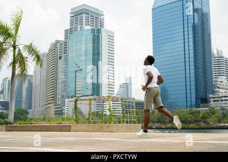 Young African man running outdoors in park with cityscape Stock Photo