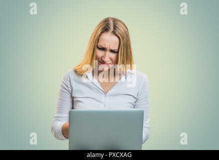 Modern blond woman frowning in misunderstanding while using laptop on gray backdrop Stock Photo