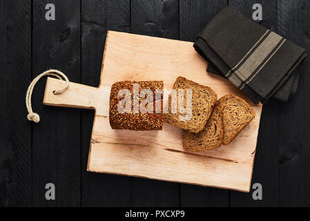Loaf of sliced whole wheat bread on cutting board over black wooden table. Stock Photo