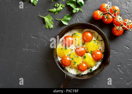Fried eggs with tomatoes in frying pan on black stone background with copy space. Top view, flat lay Stock Photo