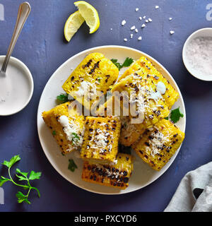 Tasty grilled corn on the cob with sauce and parmesan over blue stone background. Top view Stock Photo