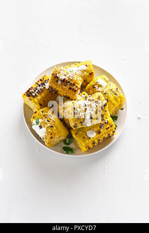 Grilled corn on cob with sauce and grated parmesan on white background with copy space. Tasty vegetarian food Stock Photo