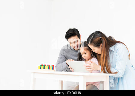 Young lovely Asian family, parents and small kid using digital tablet at home with copy space. Father and mother teaching little girl daughter Stock Photo