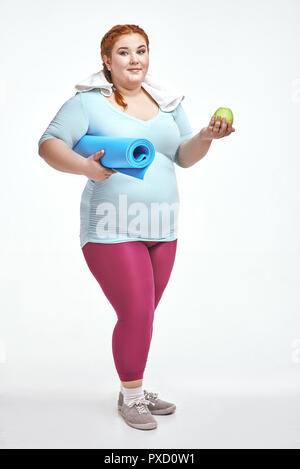 Funny picture of amusing, red haired, chubby woman on white background. Woman holding a mat. Stock Photo