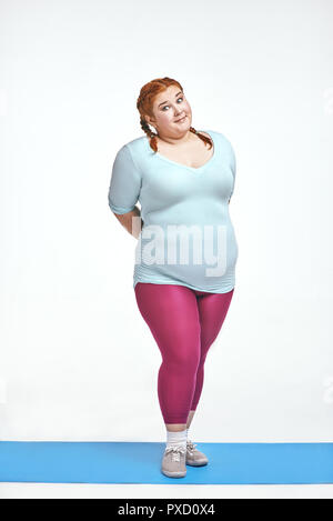 Funny picture of amusing, red haired, chubby woman on white background. Woman is shy Stock Photo
