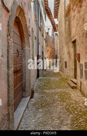 cityscape with old houses on narrow bending alley at historical touristic village on Como lake, shot in bright fall light at San Siro, Italy Stock Photo