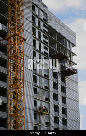 Construction of a high modern residential building of monolithic reinforced concrete and  brick on the background of clean blue sky, walls, windows an Stock Photo
