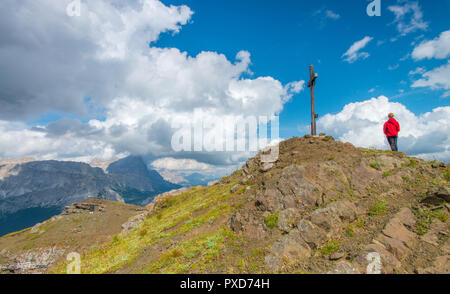 Lone hiker, traveller, tourist stands in front of a cross on top of the mountain. Praying at the wooden cross, war memorial after a hike in the summer Stock Photo