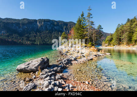 Stones on the shore of the headland over to island Braxeninsel in the Lake Eibsee surrounded by autumn forest, Bavaria, Germany Stock Photo