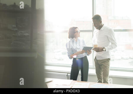 Cheerful business employees using tablet while discussing data Stock Photo
