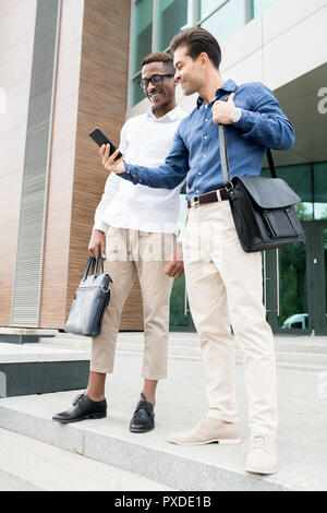 Positive multi-ethnic colleagues watching video on smartphone Stock Photo
