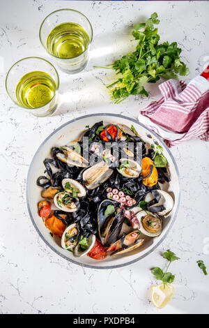 Homemade seafood Black pasta spaghetti with clams mussels octopus vongole in pan with white wine on marbled background Stock Photo
