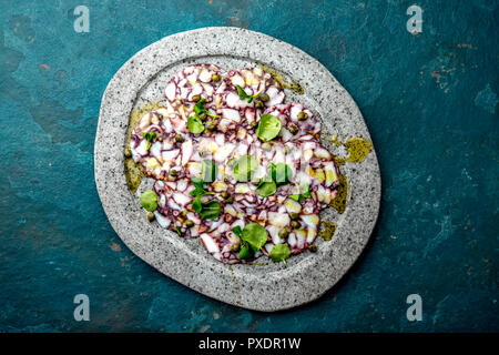 OCTOPUS CARPACCIO. Seafood Raw octopus slices with olive oil, lemon and capers on gray stone plate. Top view. blue background. Stock Photo
