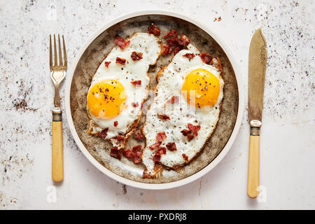 Two fresh fried eggs with crunchy crisp bacon served on rustic plate Stock Photo
