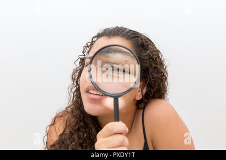 Girl looking at her eyebrow hairs by a magnifying glass. Concept of eyebrow care Stock Photo