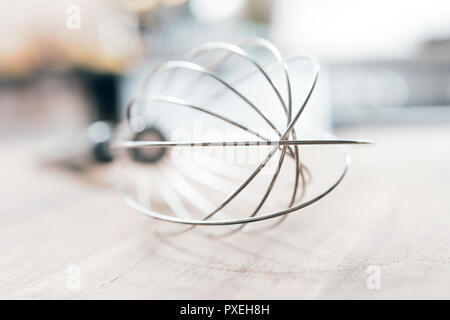 Stainless Whisk On A Wooden Table With Blurred Out Kitchen Background Stock Photo