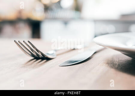 Stainless Fork, Knife And A Ceramic Plate On A Wooden Table With Blurred Out Kitchen Background Stock Photo