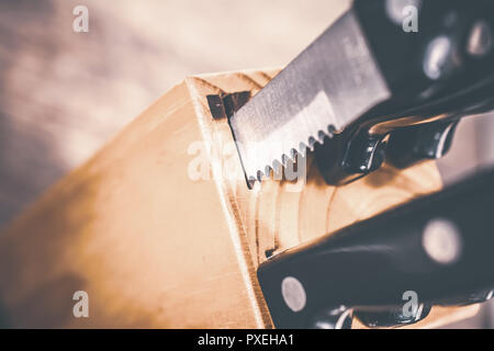 Macro Of A Jagged Steak Knife Half Pulled Out Of A Kitchen Knive Block On A Table Stock Photo