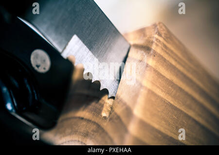 Macro Of A Jagged Steak Knife Partially Pulled Out Of A Kitchen Knive Block On A Table Stock Photo