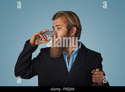 Handsome bearded well-dressed man in jacket holding tasting drinking glass of beverage whiskey alcohol isolated on grey gray studio background wall. d Stock Photo